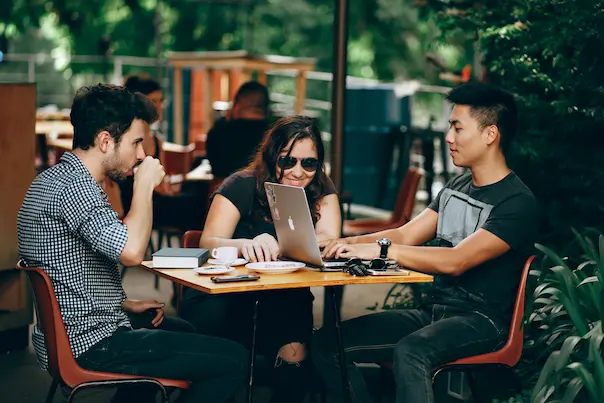 Group of people working on a desk outside looking at their laptop smiling.